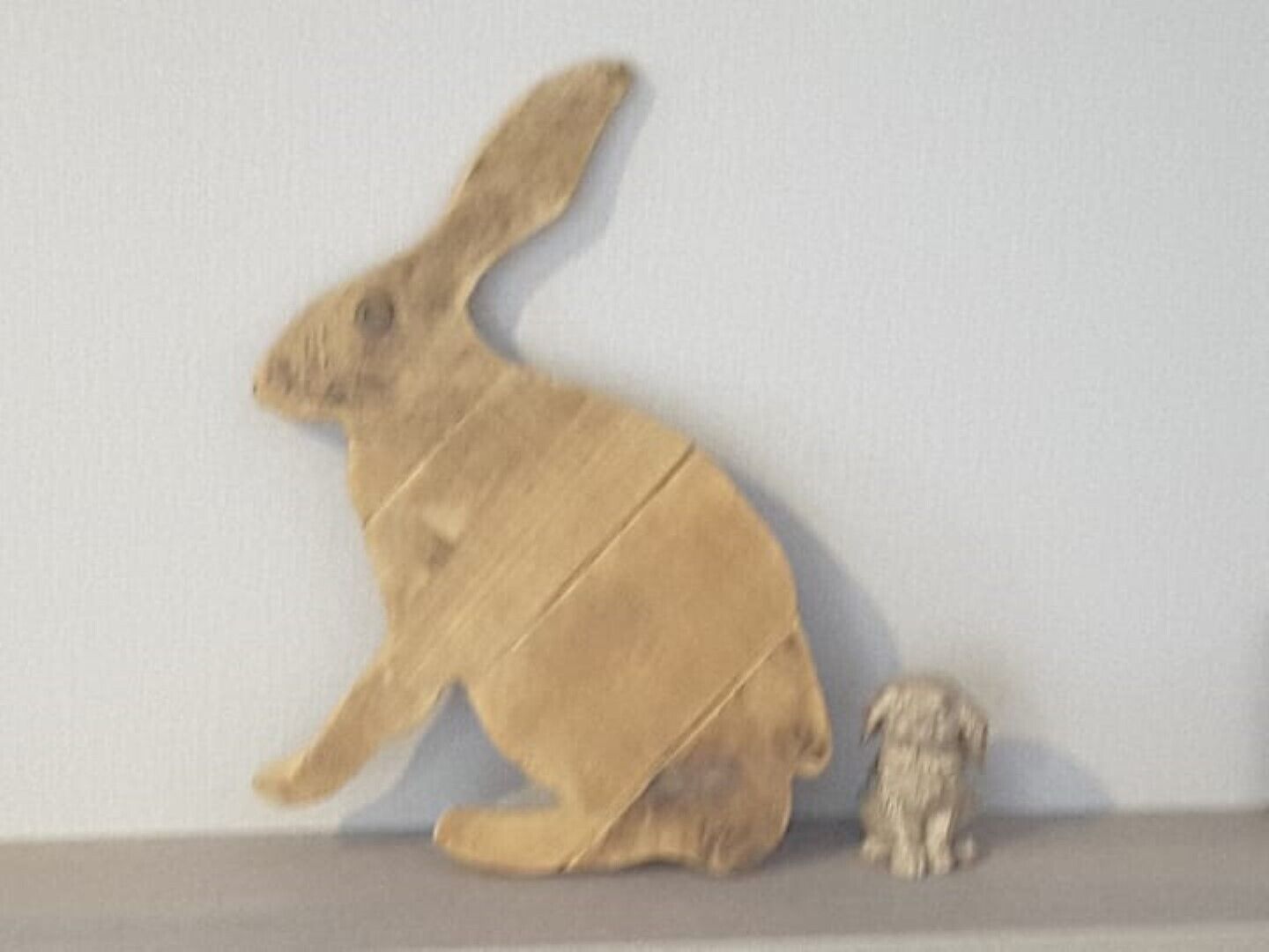 En trækaninskulptur står på en hylde foran en ensfarvet væg.