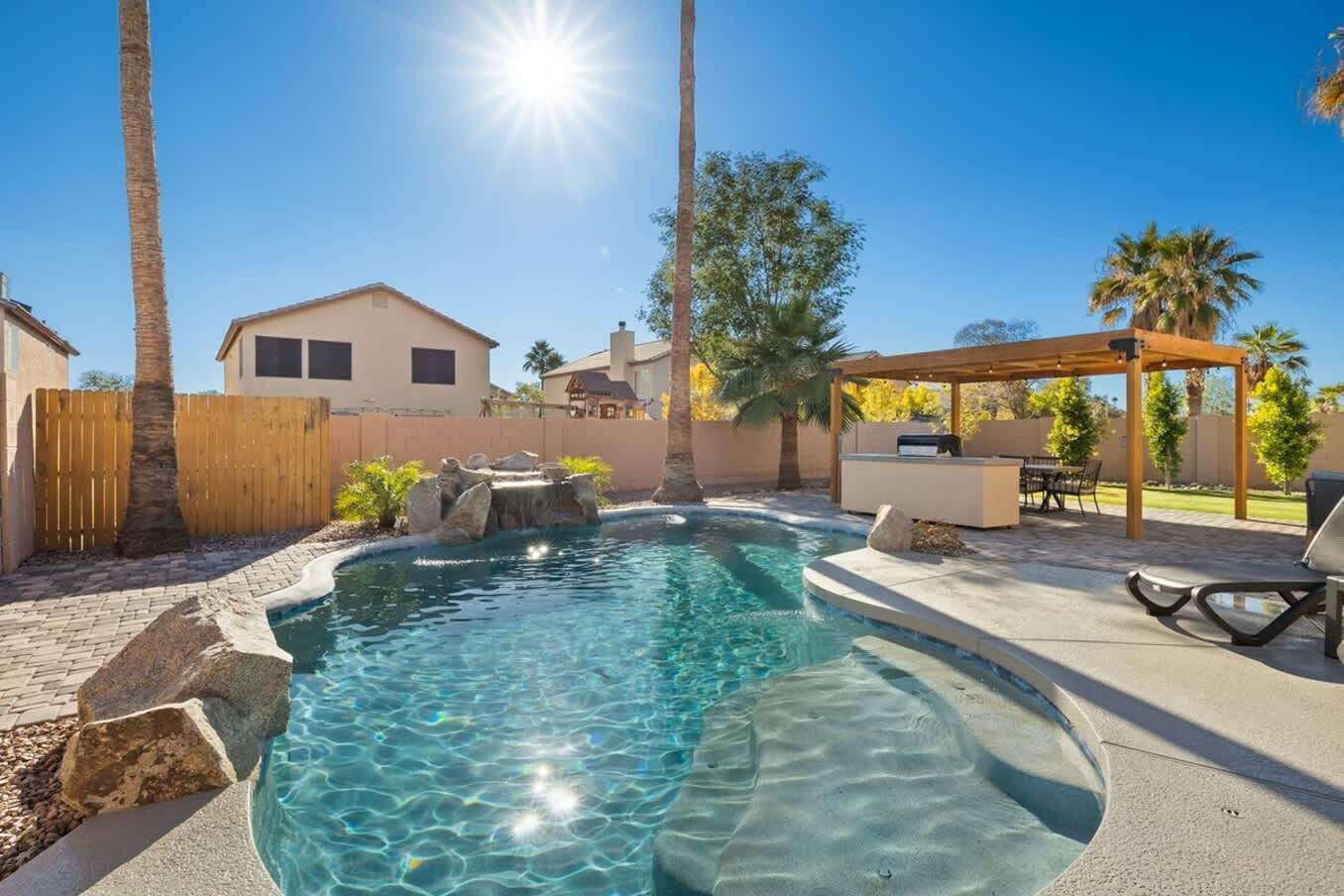 Una piscina amb un solàrium de fusta, una pèrgola i una zona de pati amb mobles d'exterior.