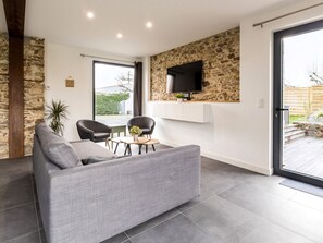 Ein modernes Wohnzimmer mit einem grauen Sofa, zwei Sesseln, einem Couchtisch und einem Flachbildfernseher, der an einer Steinwand angebracht ist.
