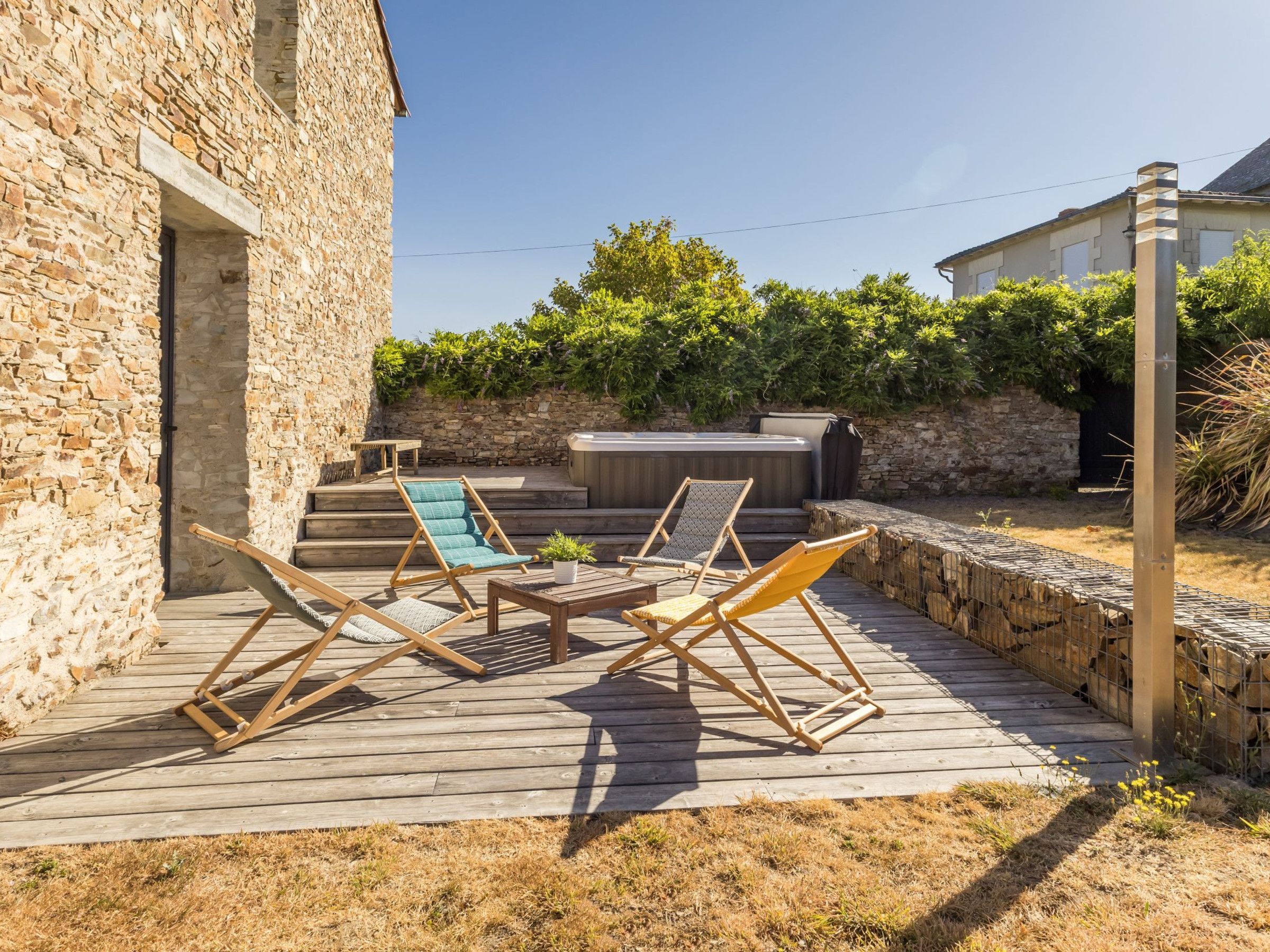 A wooden deck with outdoor furniture, a stone wall, and a hot tub.