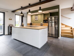 Une cuisine moderne dotée d’un îlot central, d’appareils électroménagers en acier inoxydable et de luminaires suspendus.