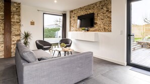 Un salon moderne avec un canapé gris, deux fauteuils, une table basse et un téléviseur à écran plat fixé à un mur en pierre.