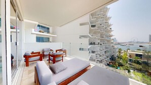 Een modern balkon met een bank, stoelen en een eettafel. Het uitzicht is op een jachthaven met boten en een reuzenrad in de verte.