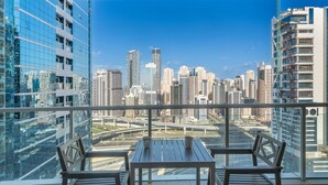 A balcony with a table and chairs, offering a view of a cityscape with high-rise buildings and a highway. - Elegant 1 Bed Escape | Walk to Metro Station | JLT (Jumeirah Lake Towers)