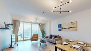 A modern living room with a dining area, large windows, and a city view. - Elegant 1 Bed Escape | Walk to Metro Station | JLT (Jumeirah Lake Towers)
