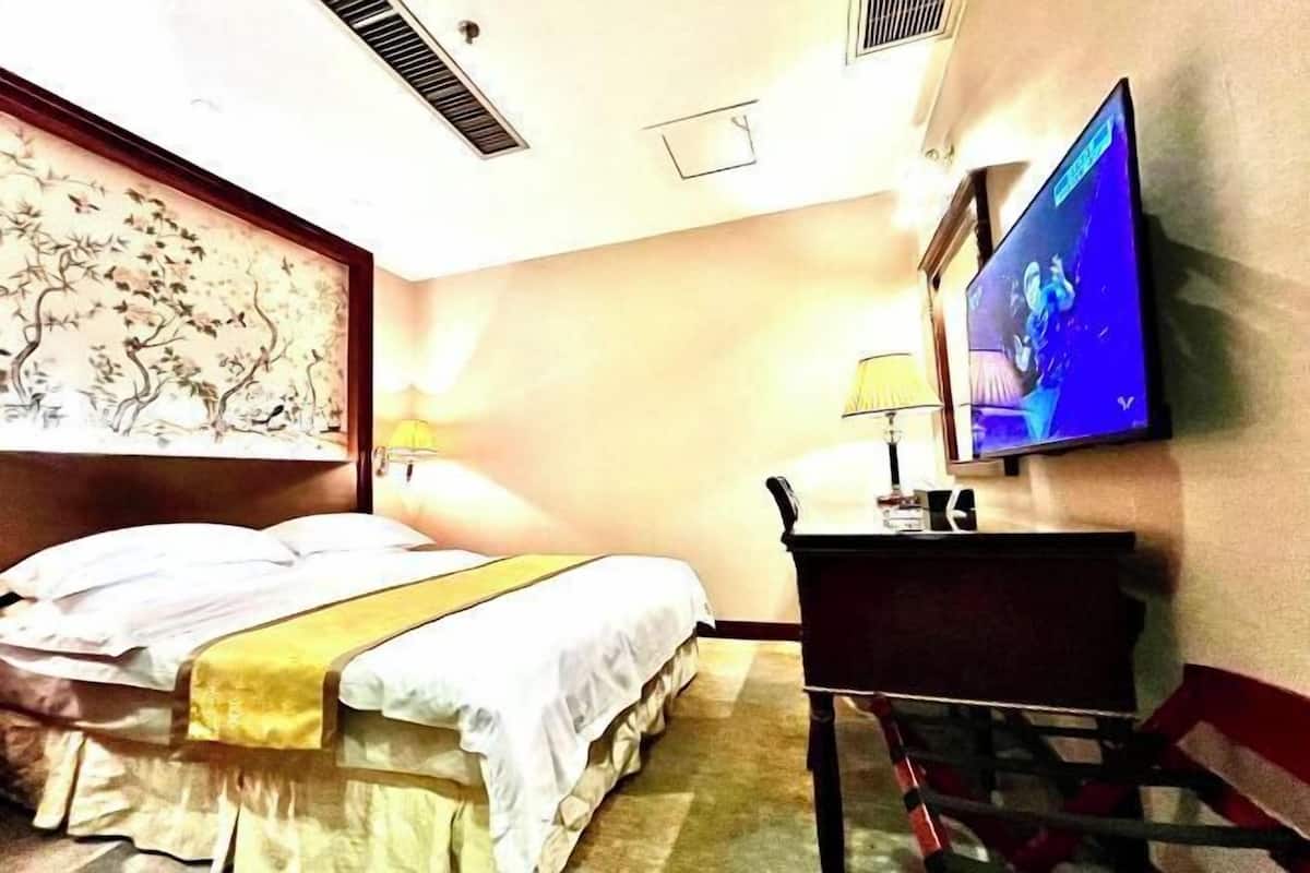 A hotel room with a bed, a desk, a chair, a television, and a wall-mounted artwork.