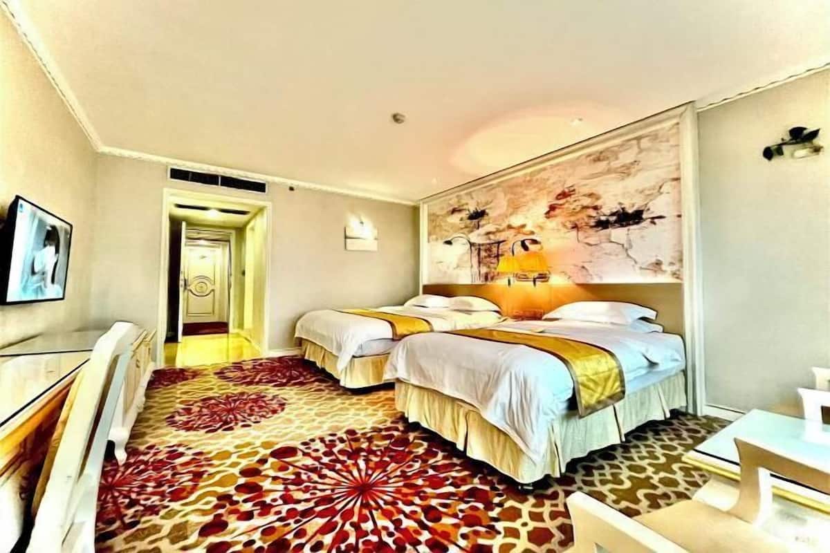 A hotel room with two beds, a large decorative rug, a painting on the wall, and a television on the left.
