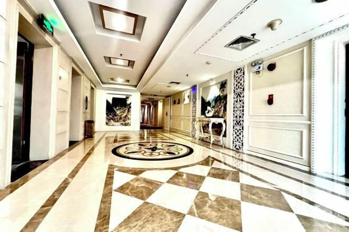 A hotel corridor with a checkered floor, a central decorative element, and a patterned wall on the right.