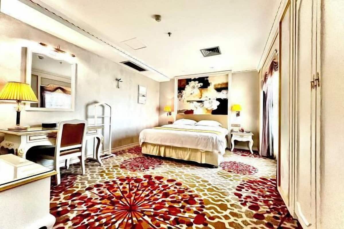 A hotel room with a bed, desk, chair, and a large floral-patterned carpet.