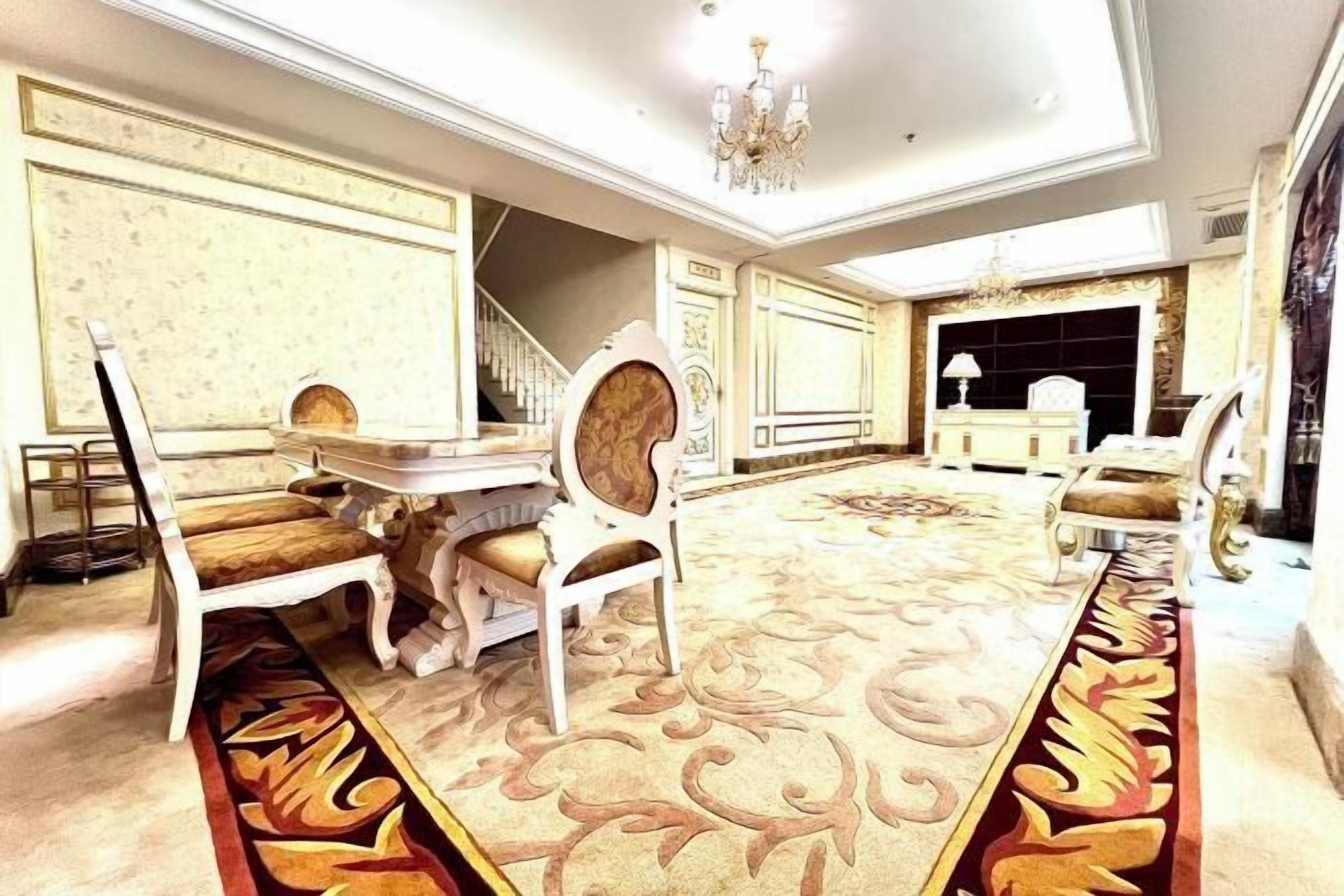 Una habitación lujosa con una imponente araña, muebles ornamentados y una alfombra estampada.