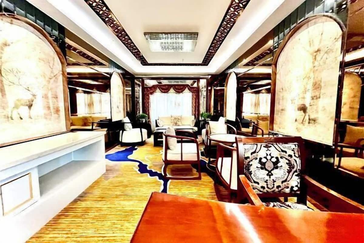 A luxurious hotel room with a large bed, a sitting area with chairs, and a long table.