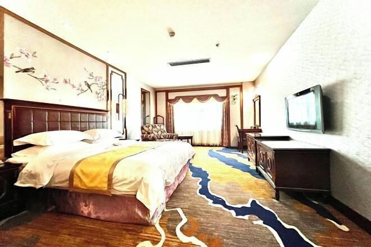 A hotel room with a bed, a desk, a chair, a television, and a decorative wall painting.