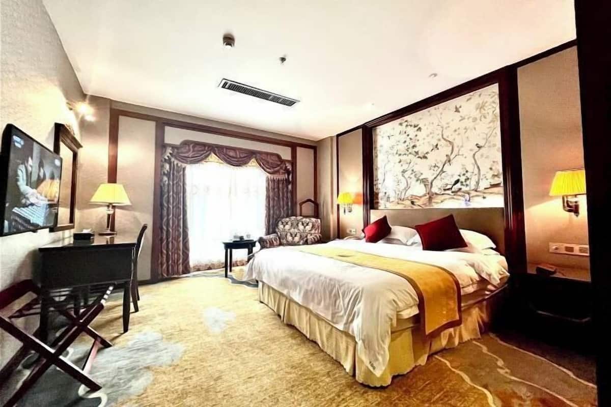 A hotel room with a bed, desk, chair, and a large painting on the wall.