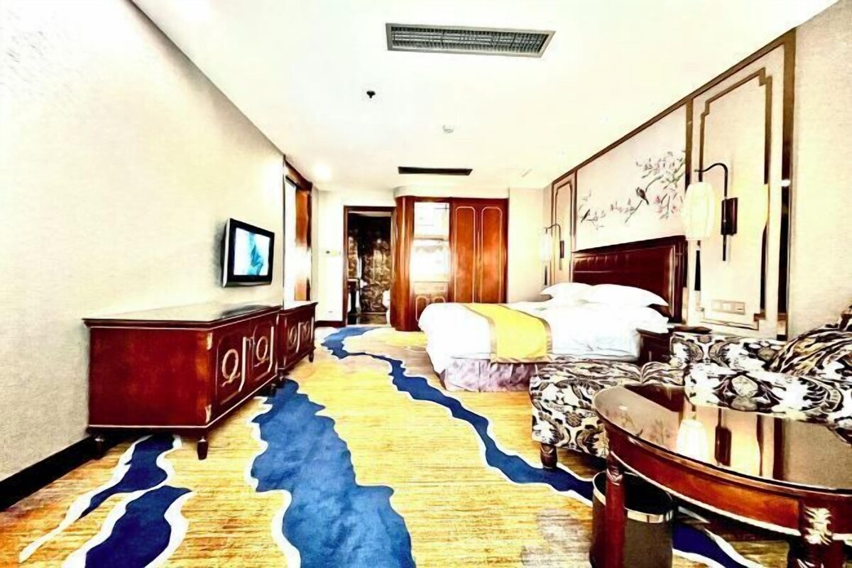 A hotel room with a bed, a sofa, a TV, and a decorative rug.