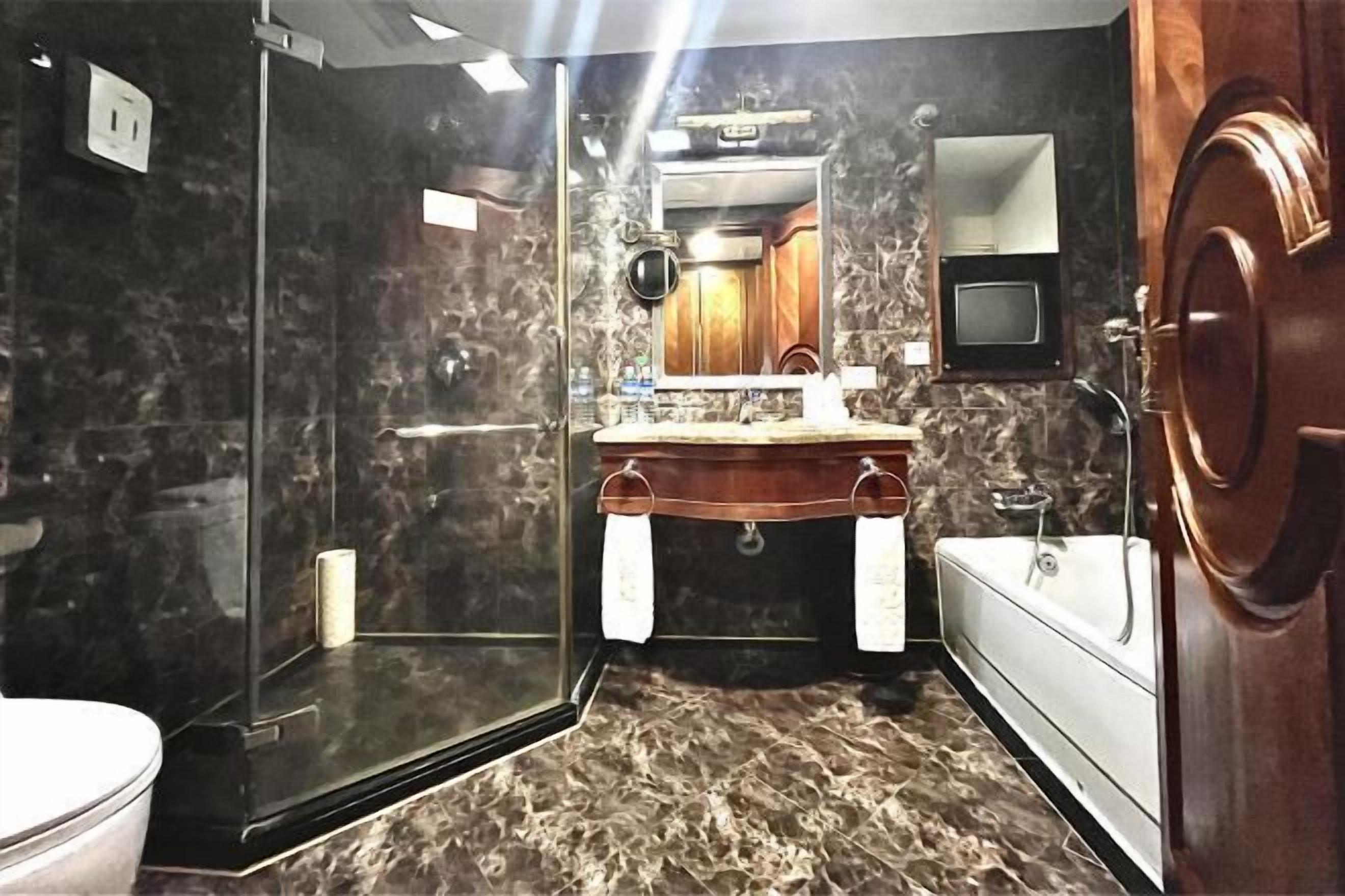 Une salle de bain dotée d’une douche à parois de verre, d’un sol carrelé en marbre, d’un meuble-lavabo en bois et d’une baignoire blanche.