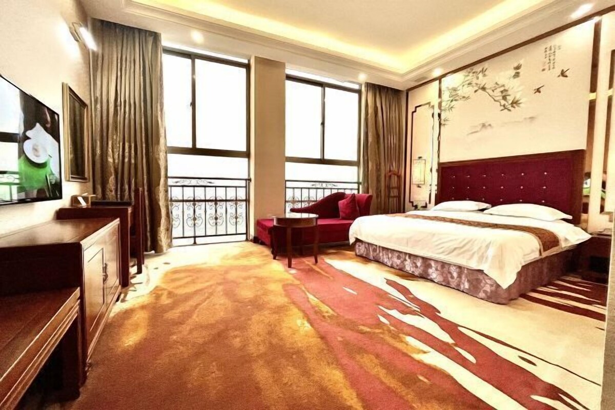 A hotel room with a large bed, a desk, a chair, and a TV.