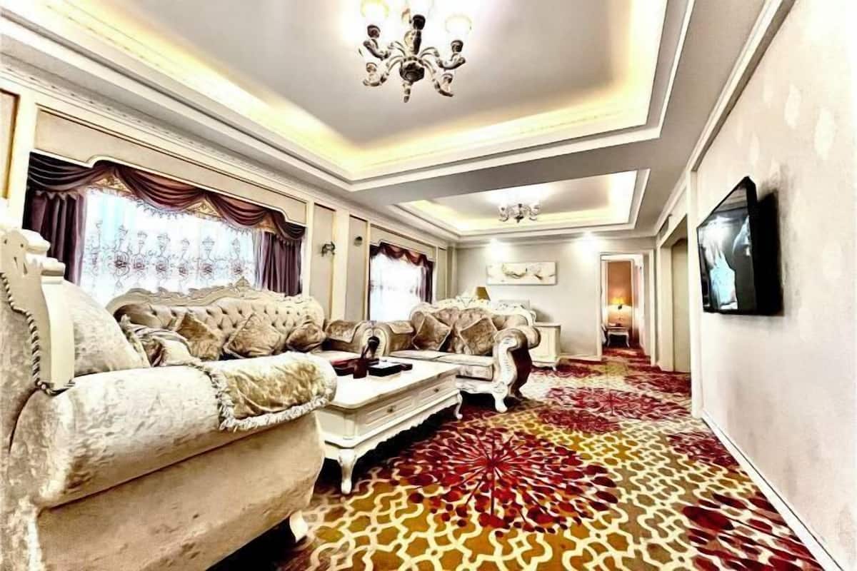 A spacious living room with a patterned carpet, elegant furniture, and a chandelier.