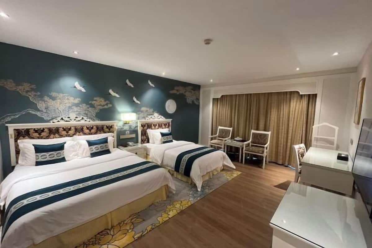 A hotel room with two beds, a desk, a chair, and a TV.