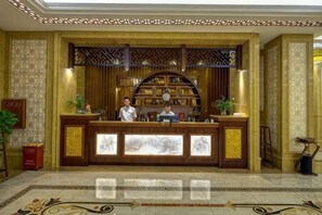 A reception desk with two staff members, a patterned wall, and a decorative ceiling.