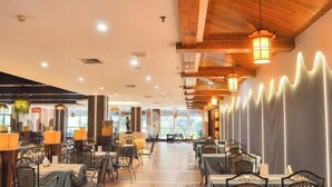 Un restaurant spacieux avec de hauts plafonds, des poutres en bois et un lustre moderne. Les tables sont disposées en forme de U, et les murs présentent un motif ondulé original.