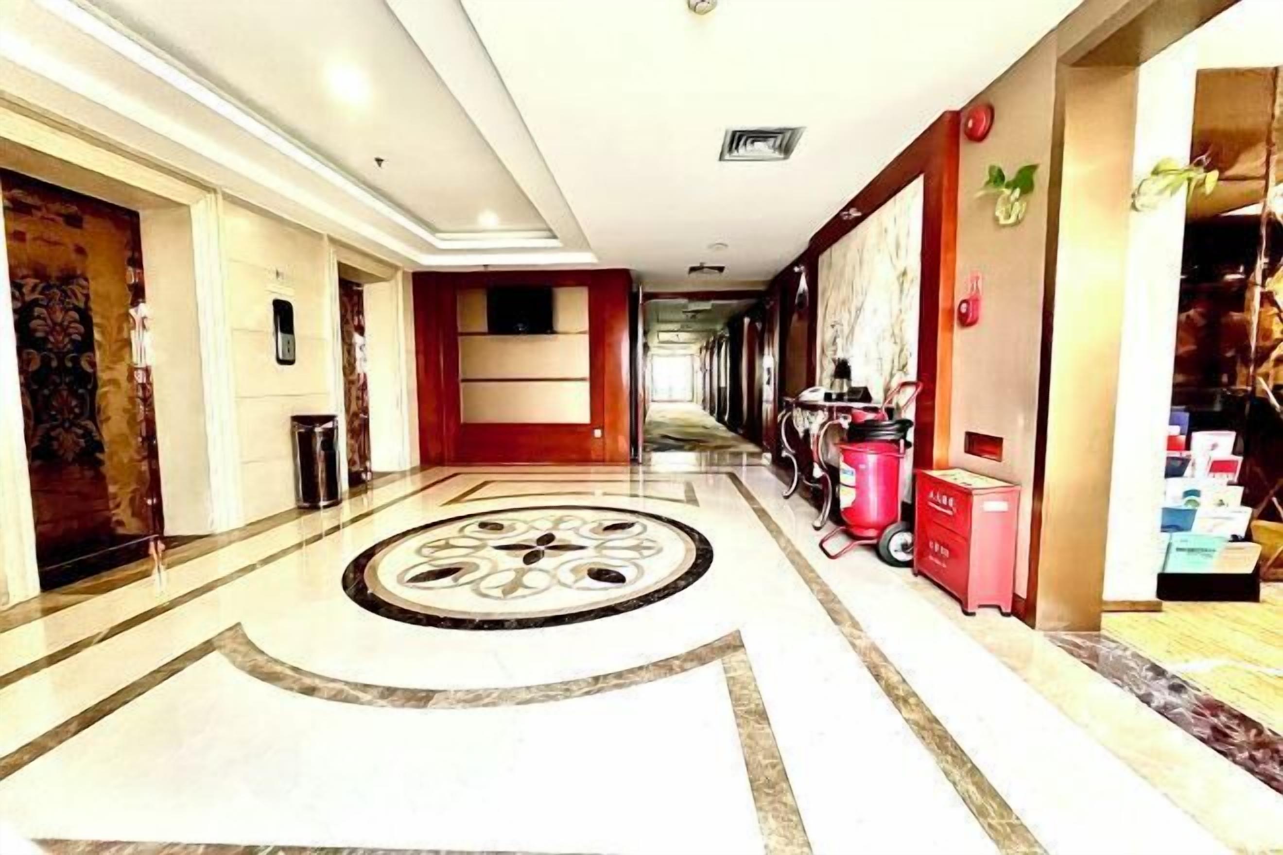 A hotel corridor with a patterned floor, a red wall, and a trash bin.