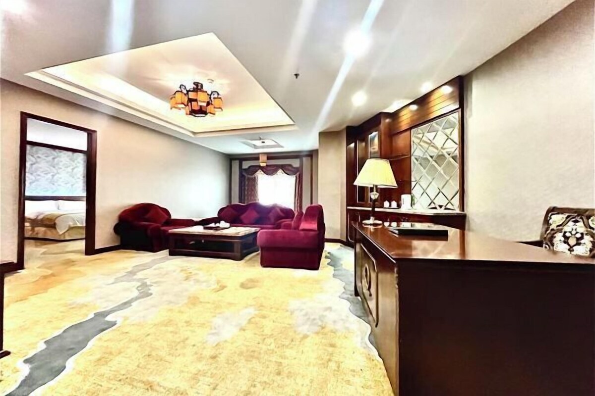 A modern living room with a sofa, a coffee table, and a TV. There is a kitchen area with a counter and a lamp.