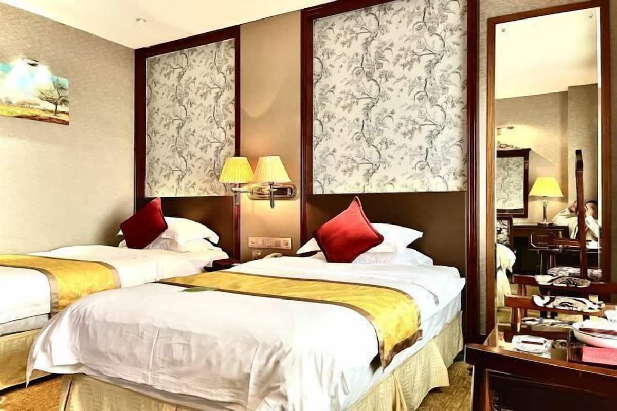 A hotel room with two beds, a large mirror, and a desk with a lamp.