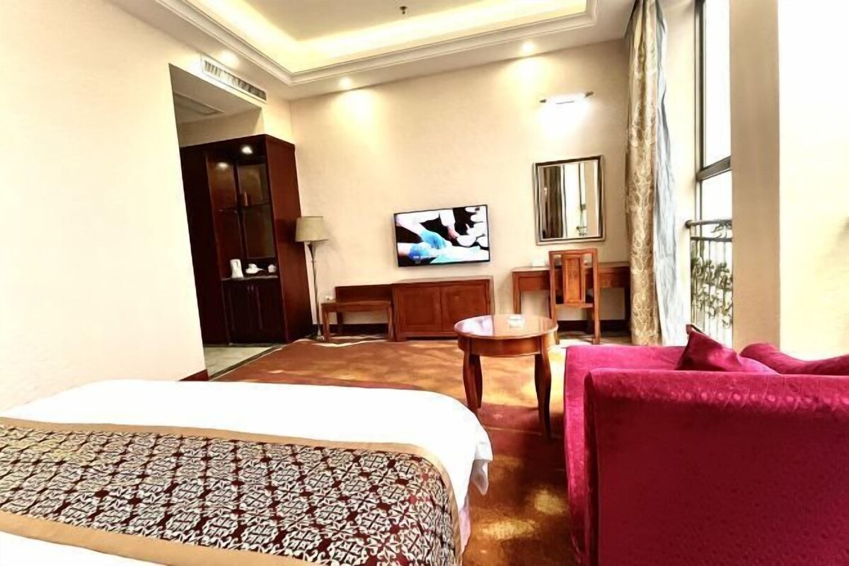 A hotel room with a large bed, a red sofa, a TV on the wall, and a small table.