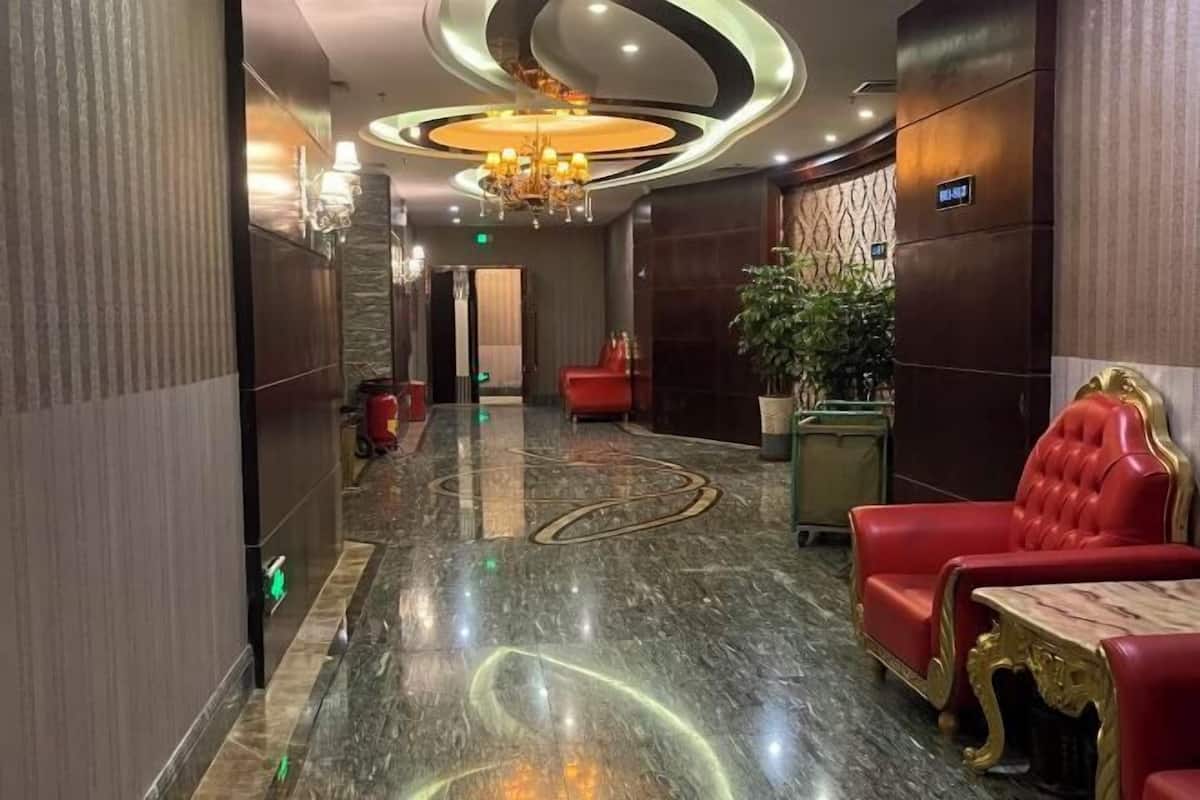 A lobby with a marble floor, red leather chairs, a chandelier, and a potted plant.