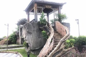 A traditional pavilion with a staircase leading up to it, surrounded by rock formations and greenery. - Huang Du Big Hotel (Shantou)