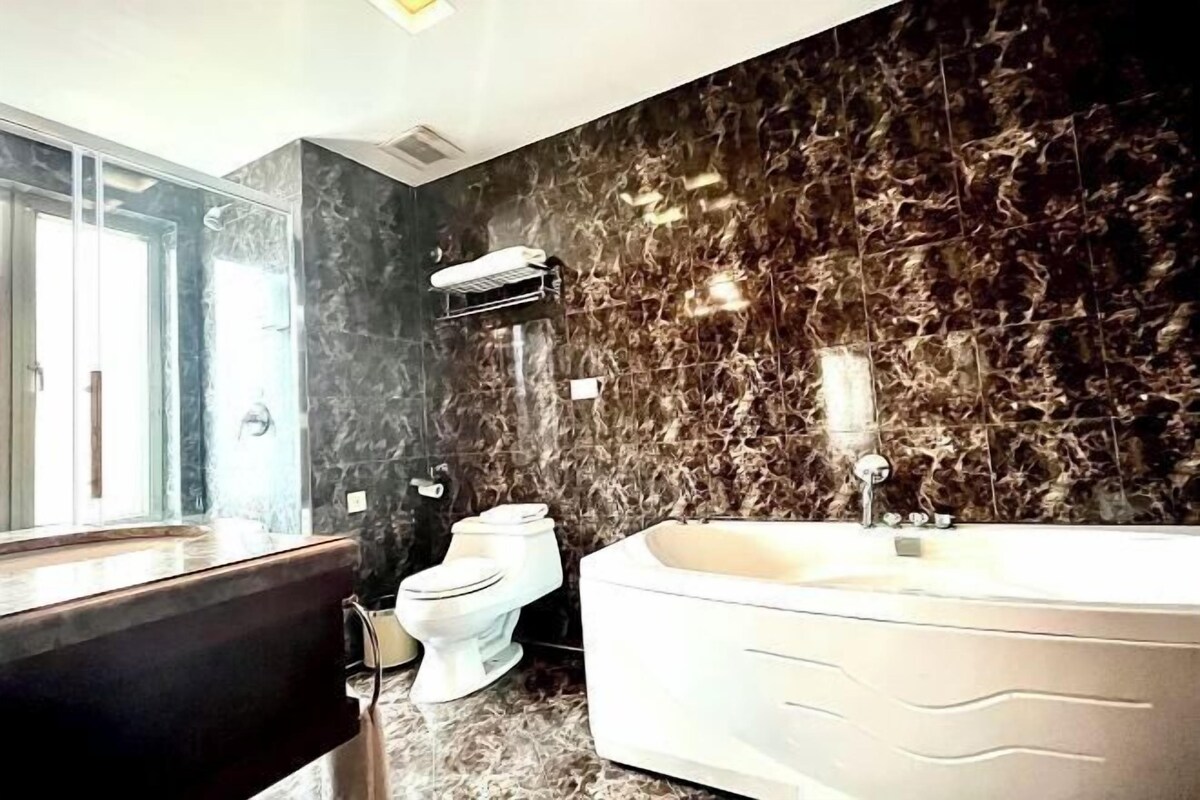 A bathroom with a marble wall, a bathtub, and a toilet.