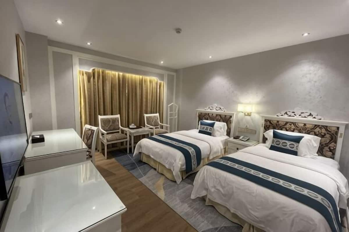 A hotel room with two beds, a desk, a chair, a TV, and a curtain.