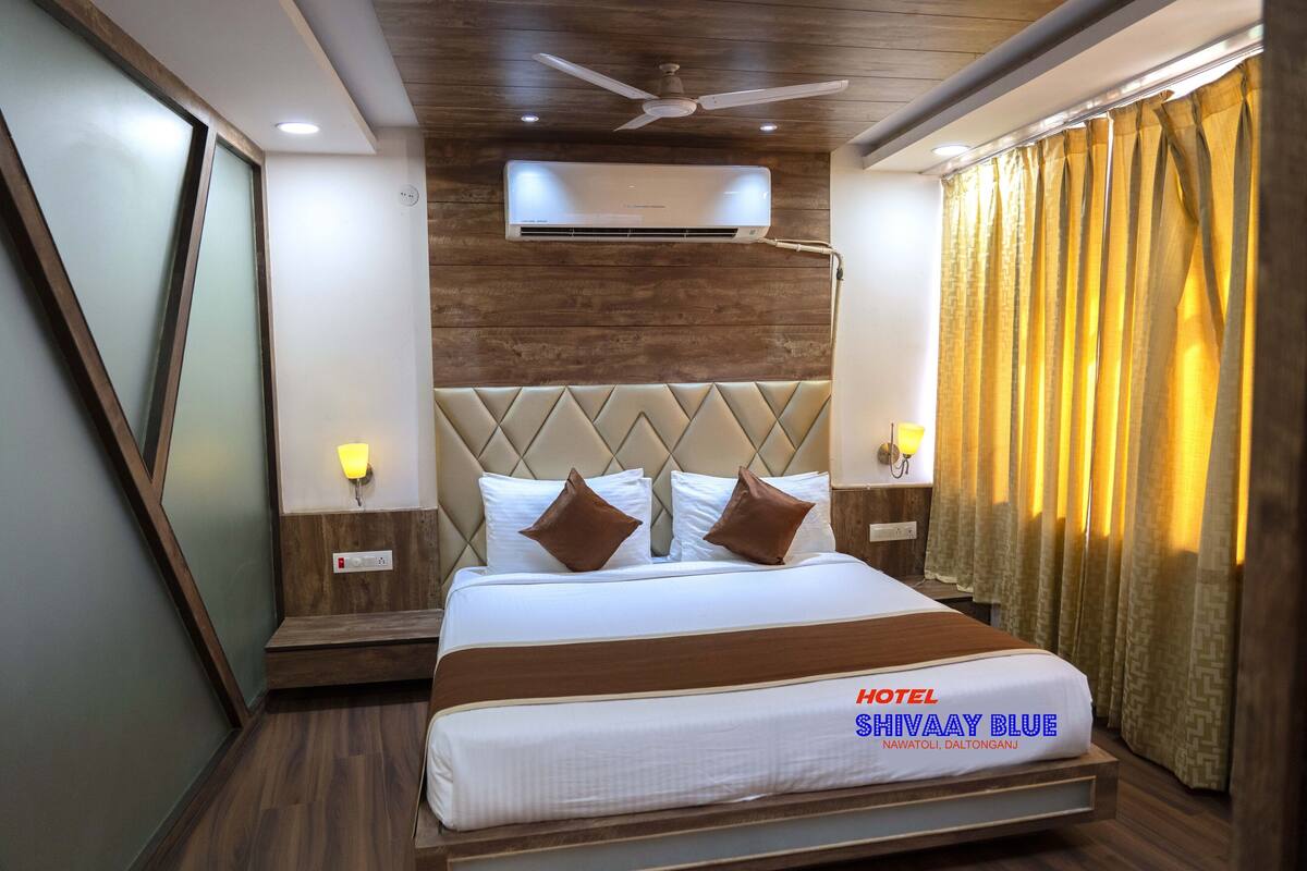 Una habitación de hotel con cama, ventilador de techo, aire acondicionado y cortinas.