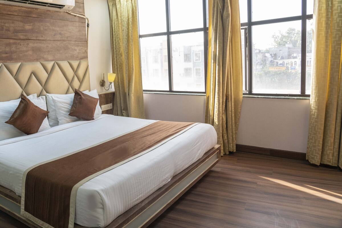 Habitación de hotel con una cama grande, cabecera de madera y vistas a la ciudad a través de amplios ventanales.