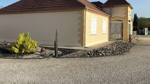A building with a beige facade, a brown roof, and a small garden area with a bush and a wooden post. - Pretty house with swimming pool in Périgord (Pazayac)