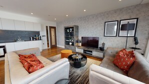 Ein modernes Wohnzimmer mit einer Couch, einem Couchtisch und einem Fernseher. Es gibt eine Küchenzeile mit Schränken und einer Spüle.