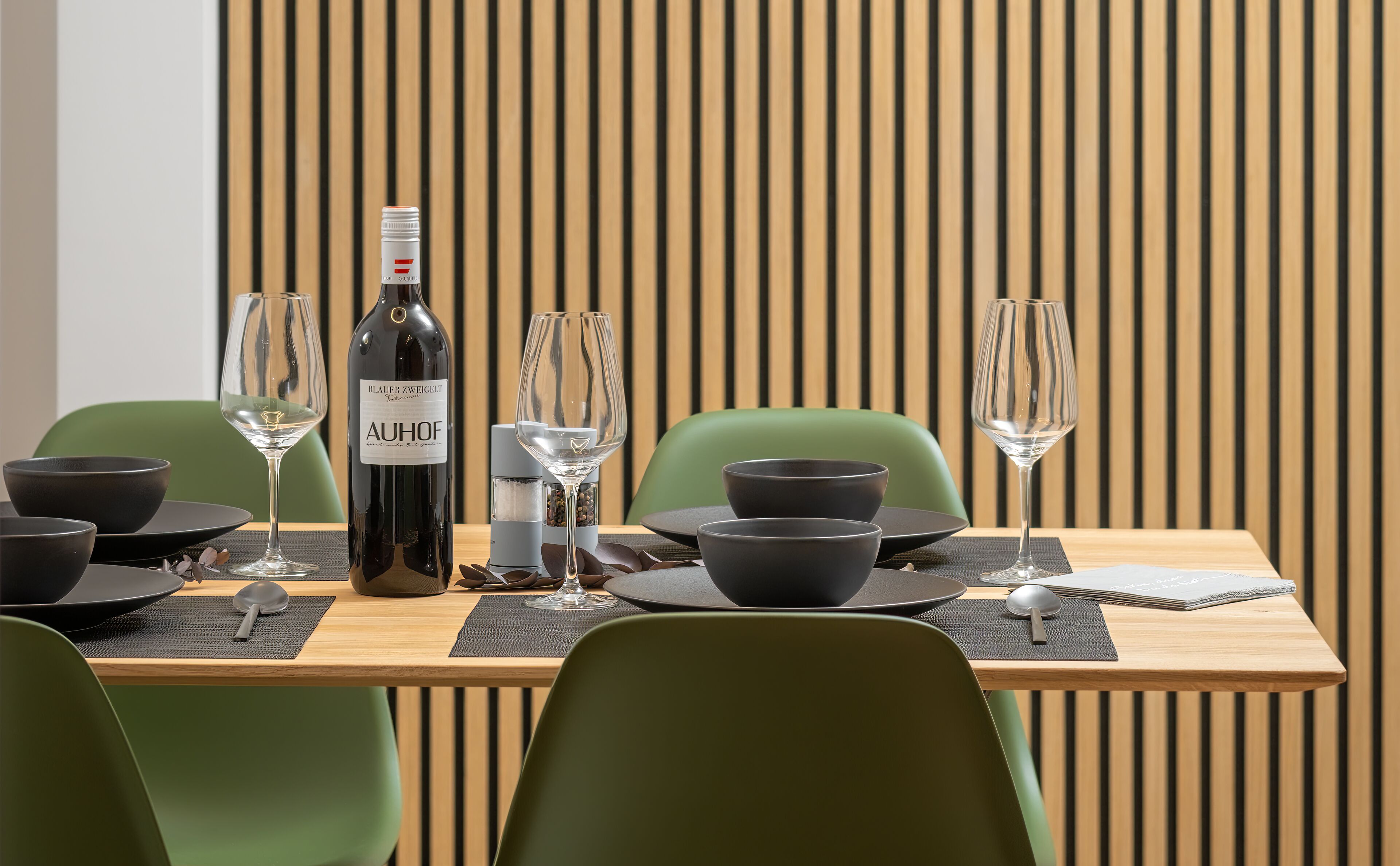 Une table à manger dressée avec des verres à vin, une bouteille de vin et des bols noirs.