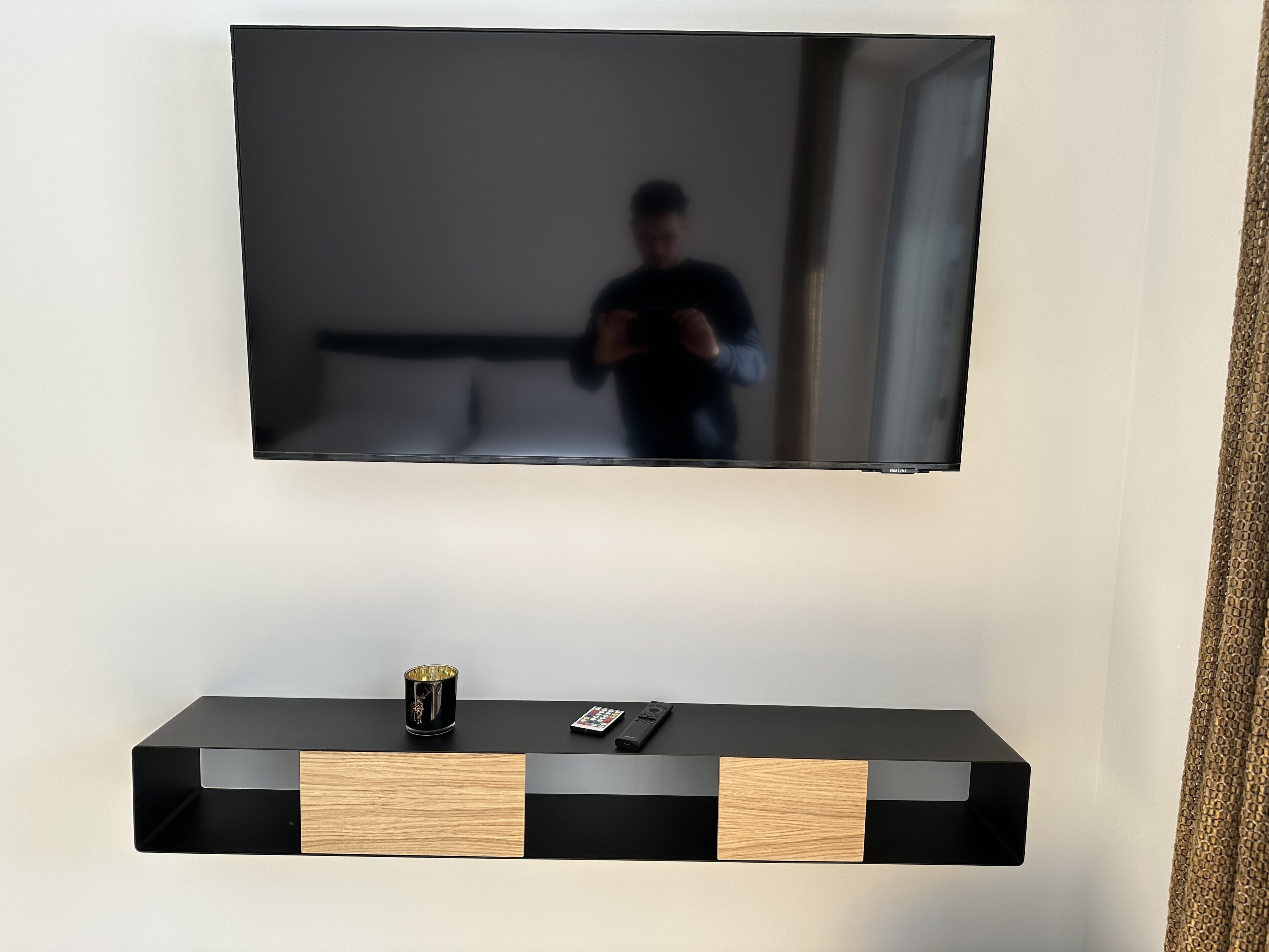 A flat-screen TV mounted on a wall above a black and wood console with a remote and a decorative item.