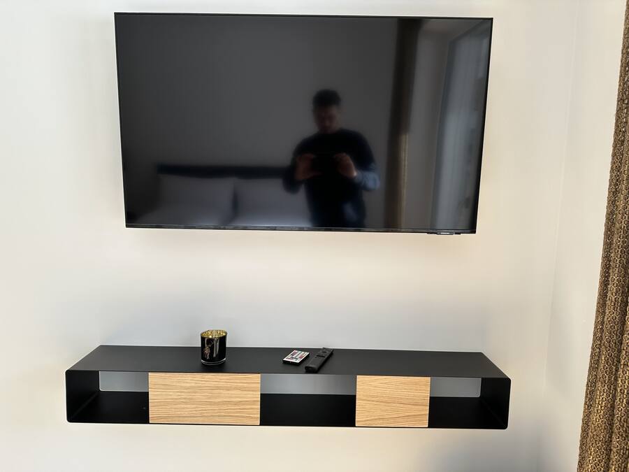 Un televisor de pantalla plana montado en la pared sobre un mueble negro de madera con un control remoto y un adorno.