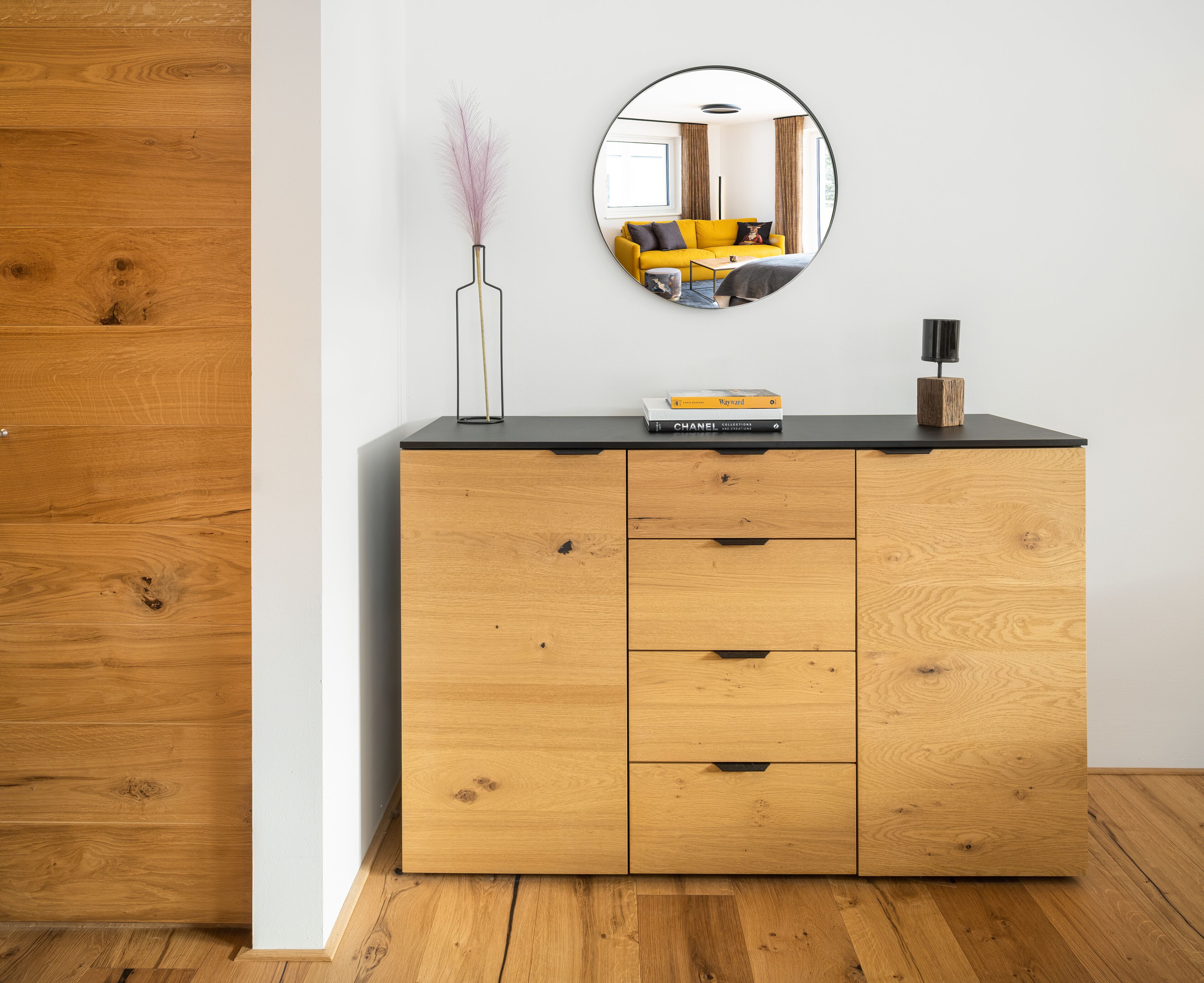 A wooden dresser with a mirror above it, a vase with dried plants, and a few books on top.