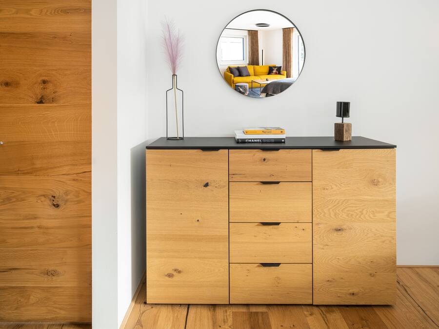 A wooden dresser with a mirror above it, a vase with dried plants, and a few books on top.
