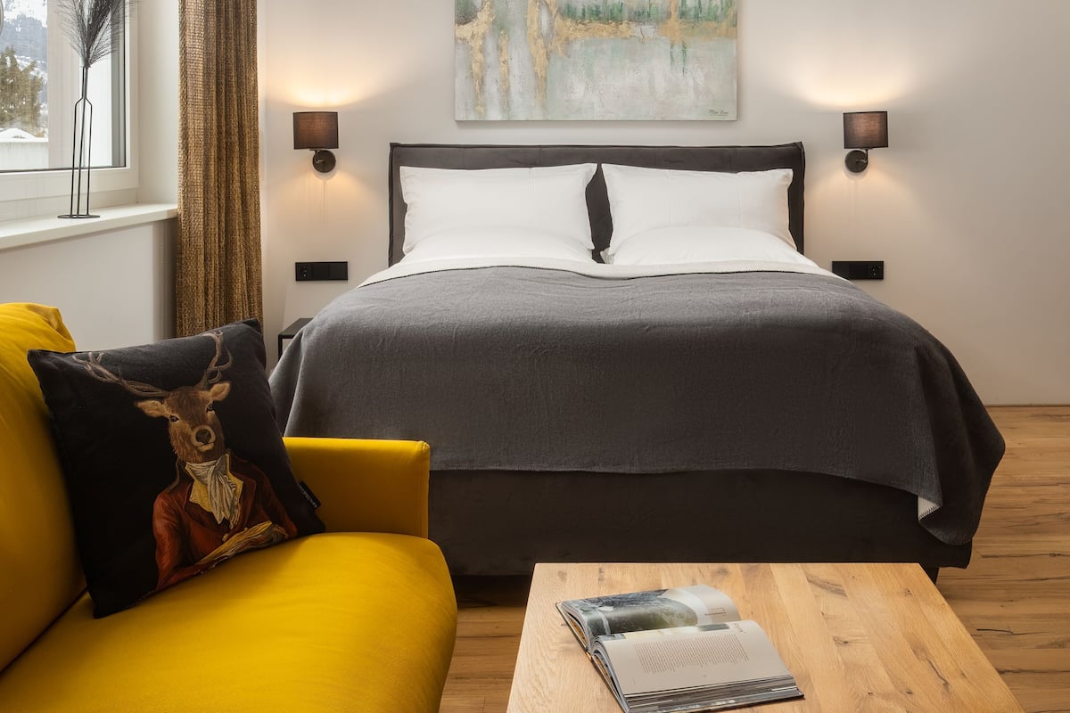 Un dormitorio moderno con cama, lámparas de noche, un cuadro, una ventana con cortinas, un sofá y una mesa de centro.