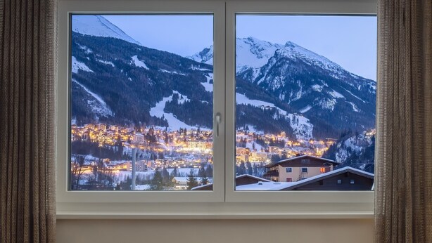 A window with a view of a snow-covered mountain and a lit-up town below. - Auhof (Bad Gastein)