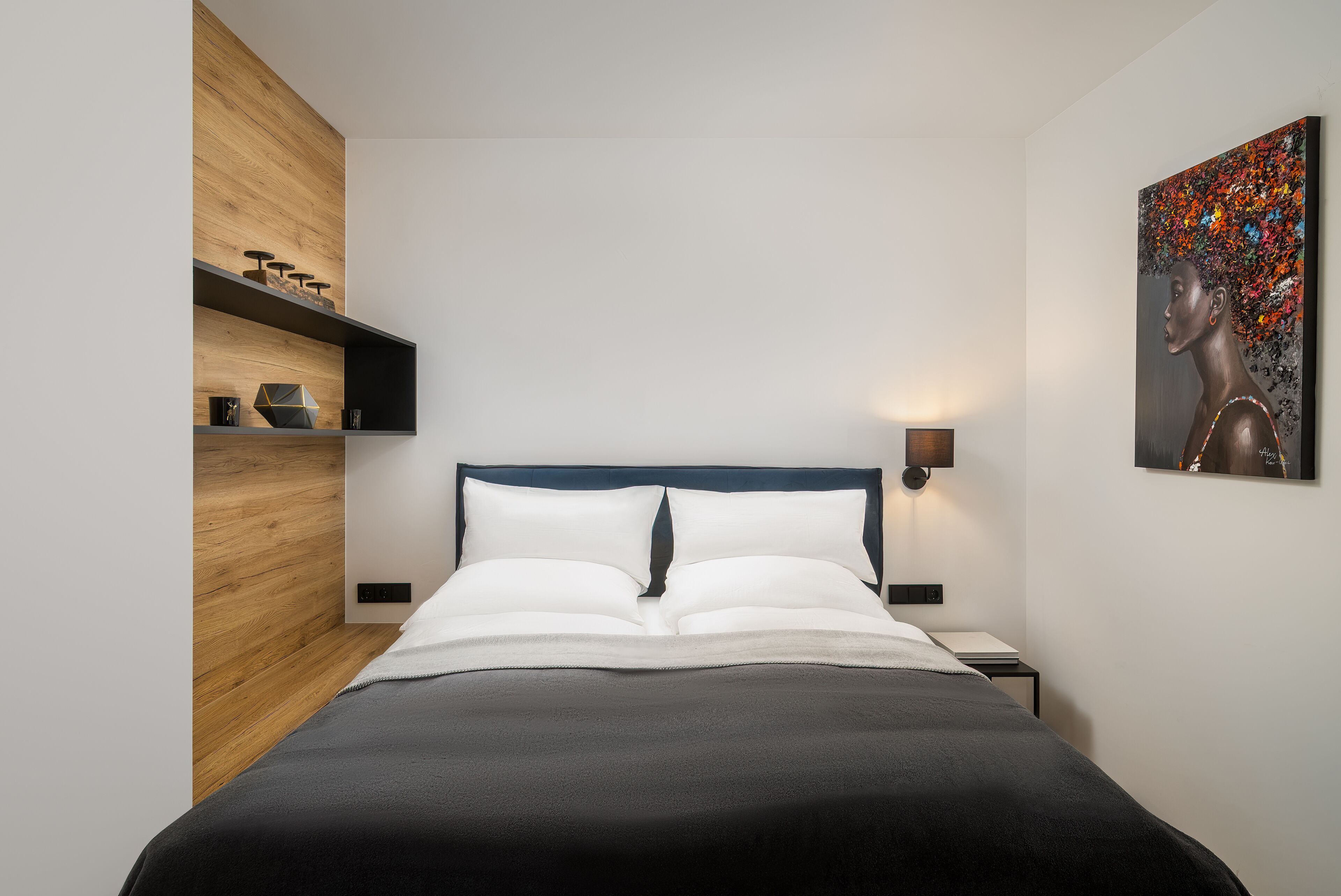 A modern bedroom with a bed, wooden paneling, a nightstand, and a wall-mounted lamp.