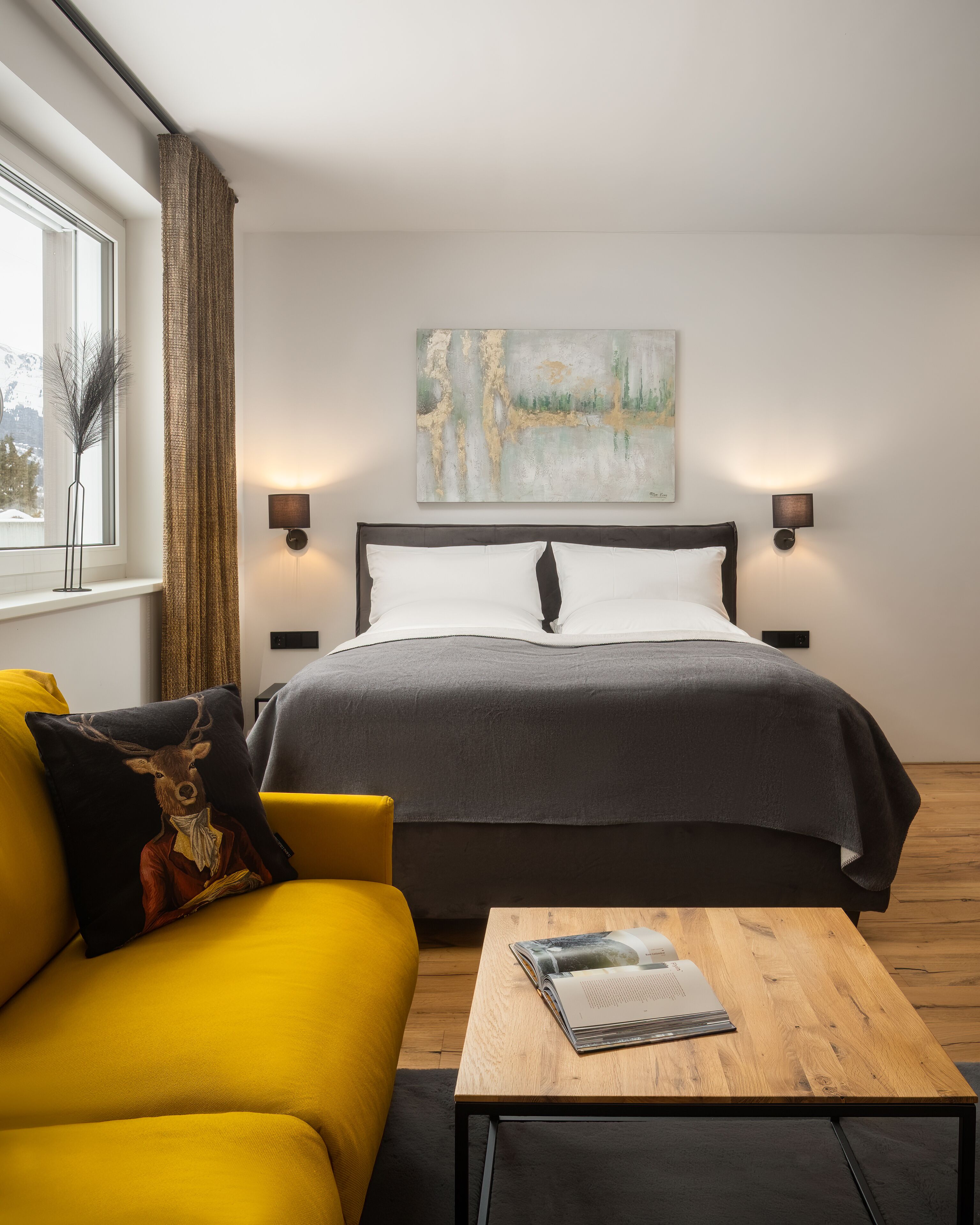 A modern bedroom with a large bed, a yellow sofa, a wooden coffee table, and a painting on the wall.