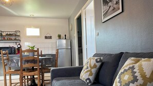 Un salon chaleureux avec un canapé gris, des coussins à motifs et un coin repas comprenant une chaise et une table en bois.
