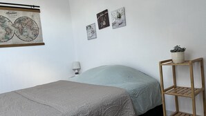 Une chambre à coucher avec un lit, une table de chevet, une lampe fixée au mur, une carte et une petite étagère avec une plante.