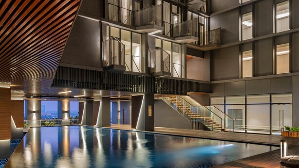 A modern indoor swimming pool with a wooden deck, a staircase, and a view of the cityscape. - Herloom BSD (Gading Serpong)
