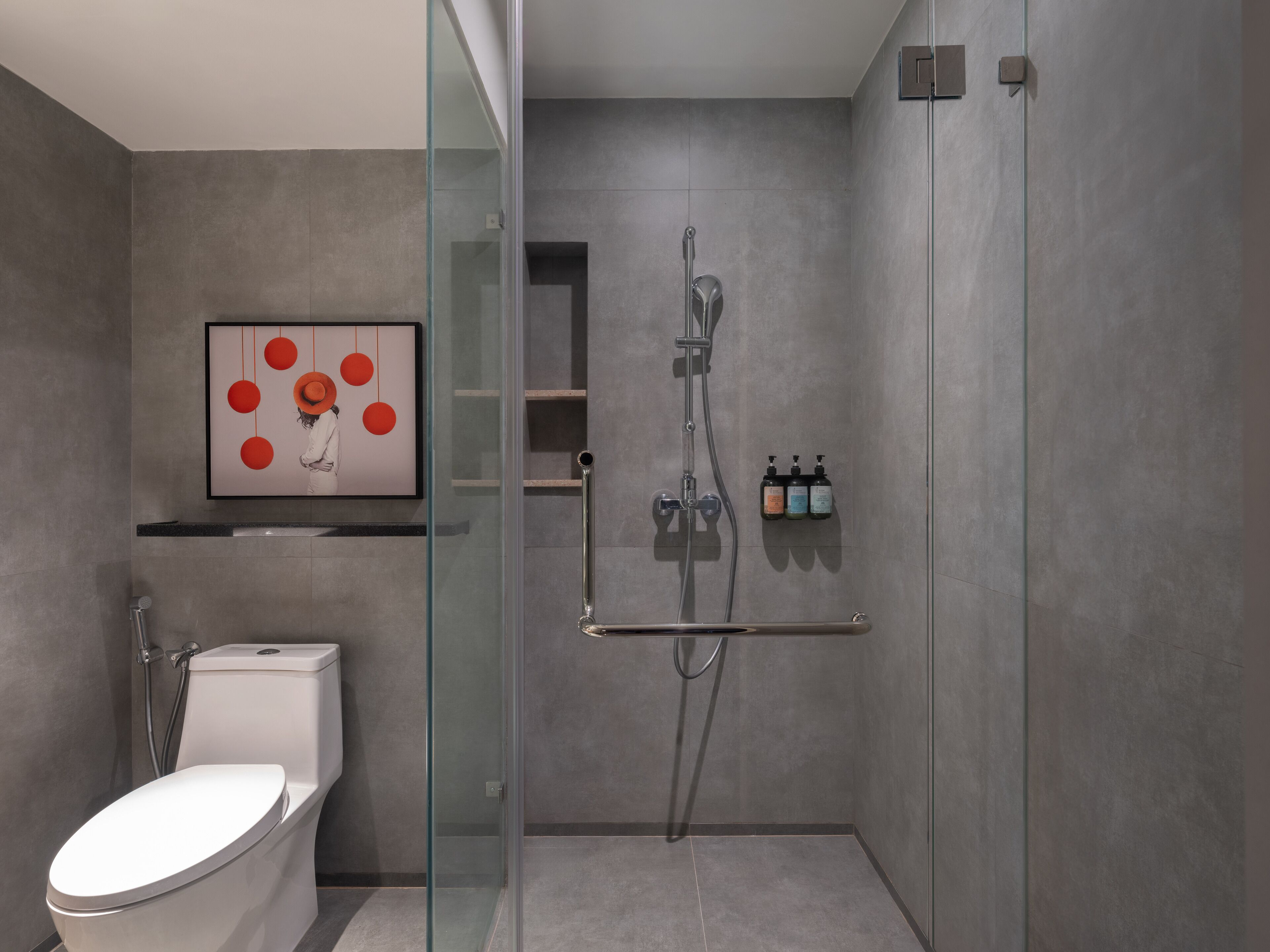 Un baño moderno con ducha de vidrio, un inodoro y una obra de arte enmarcada en la pared.