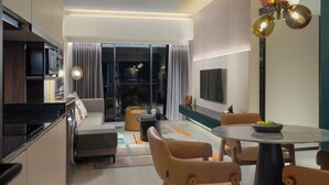 A modern living room with a sofa, dining table, and chairs. There is a TV mounted on the wall and a window with curtains. - Herloom BSD (Gading Serpong)